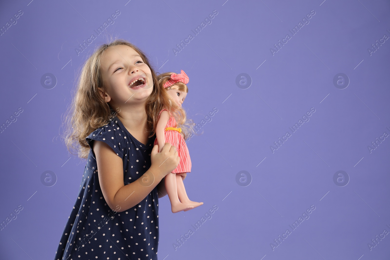 Photo of Cute little girl with doll on purple background. Space for text