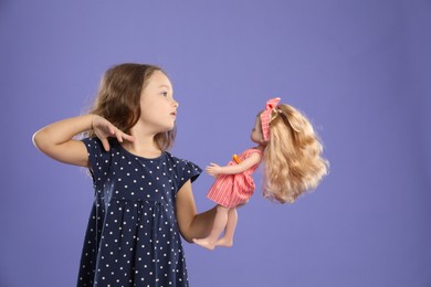 Photo of Cute little girl with doll on purple background. Space for text