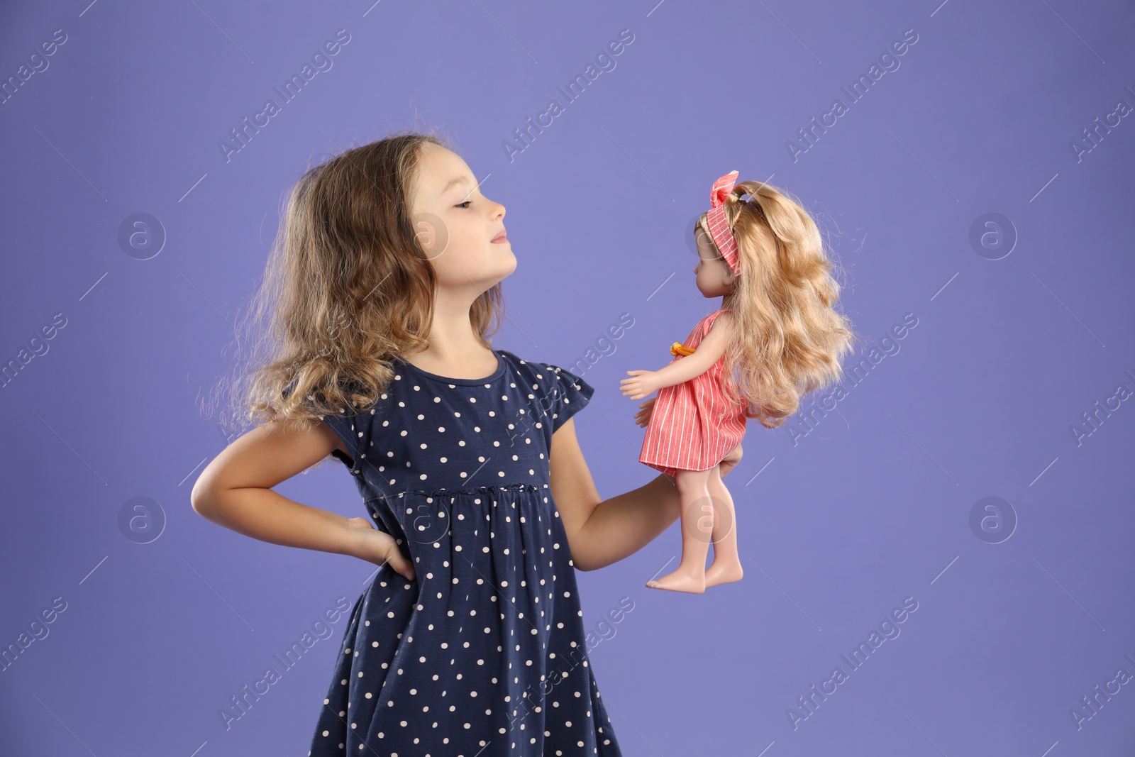 Photo of Cute little girl with doll on purple background