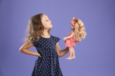 Photo of Cute little girl with doll on purple background