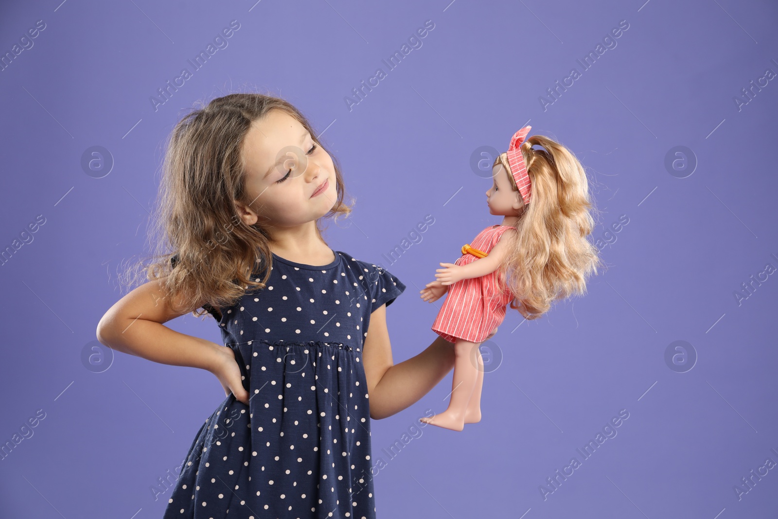 Photo of Cute little girl with doll on purple background