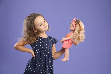 Photo of Cute little girl with doll on purple background