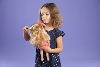 Photo of Cute little girl brushing doll's hair on purple background