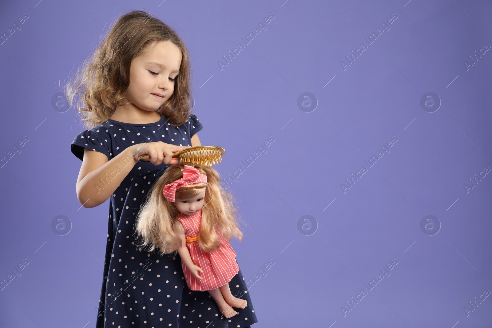 Photo of Cute little girl brushing doll's hair on purple background. Space for text