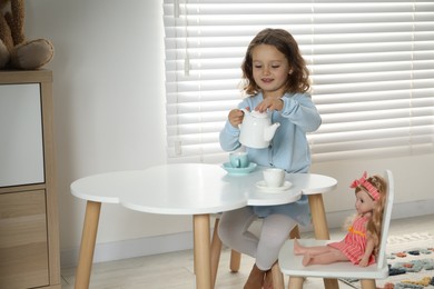 Photo of Cute little girl playing tea party with doll at white table in room