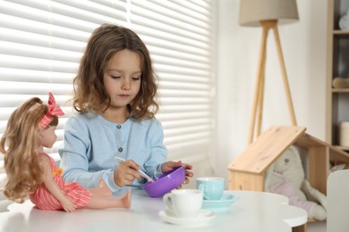 Photo of Cute little girl playing with doll and toy dishware at table in child's room