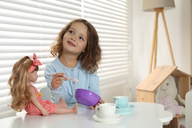 Photo of Cute little girl playing with doll and toy dishware at table in child's room