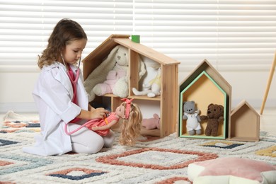 Photo of Cute little girl playing doctor with doll at home