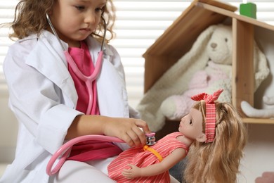 Photo of Cute little girl playing doctor with doll at home