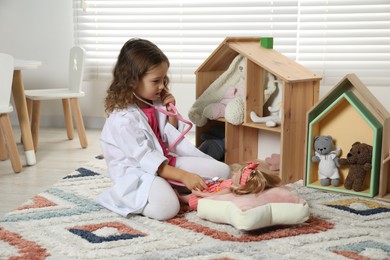 Photo of Cute little girl playing doctor with doll at home