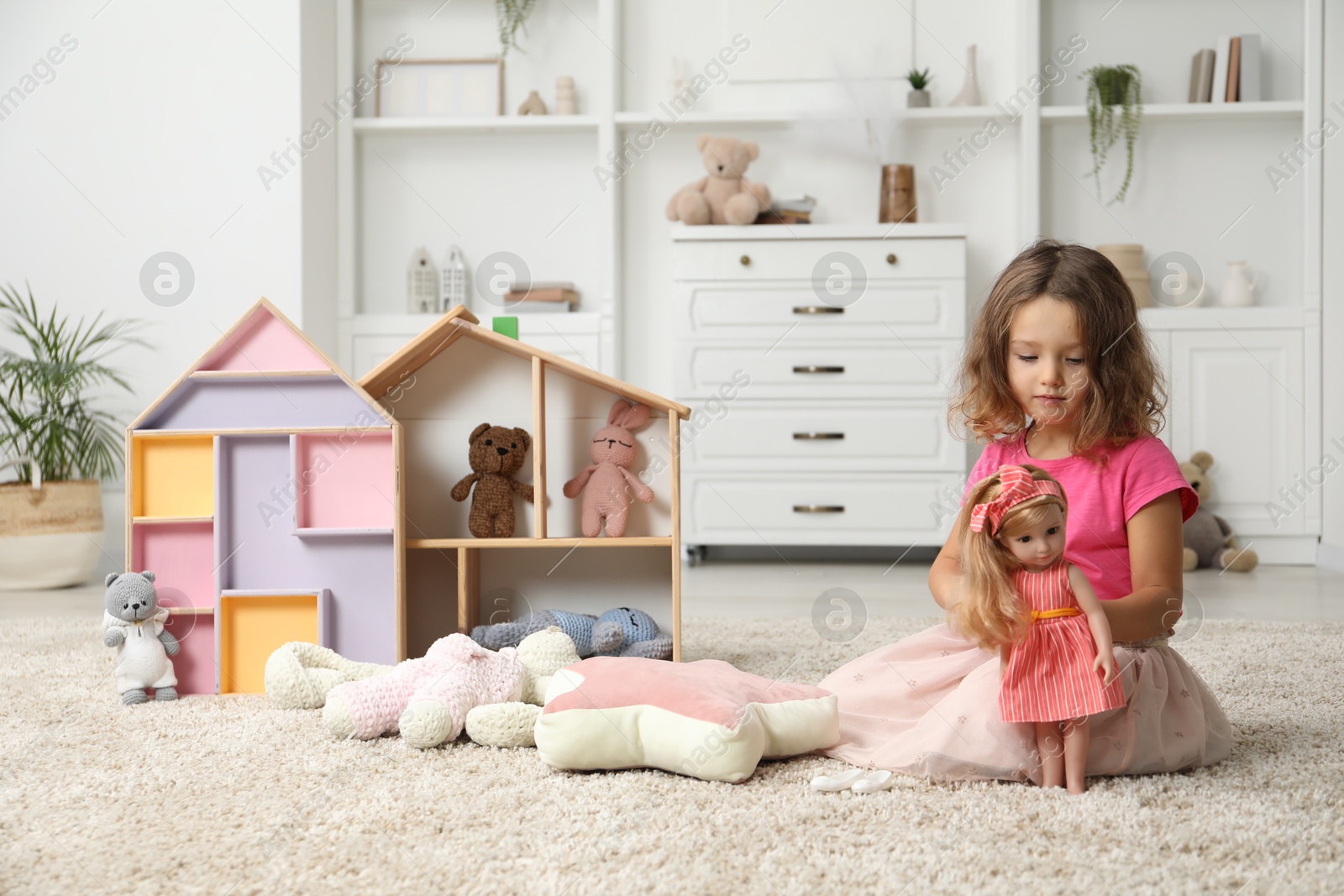 Photo of Cute little girl playing with doll and other toys on floor at home