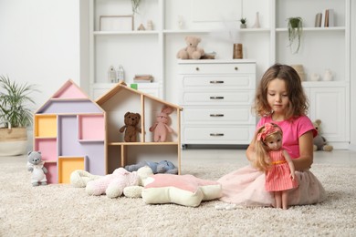 Photo of Cute little girl playing with doll and other toys on floor at home