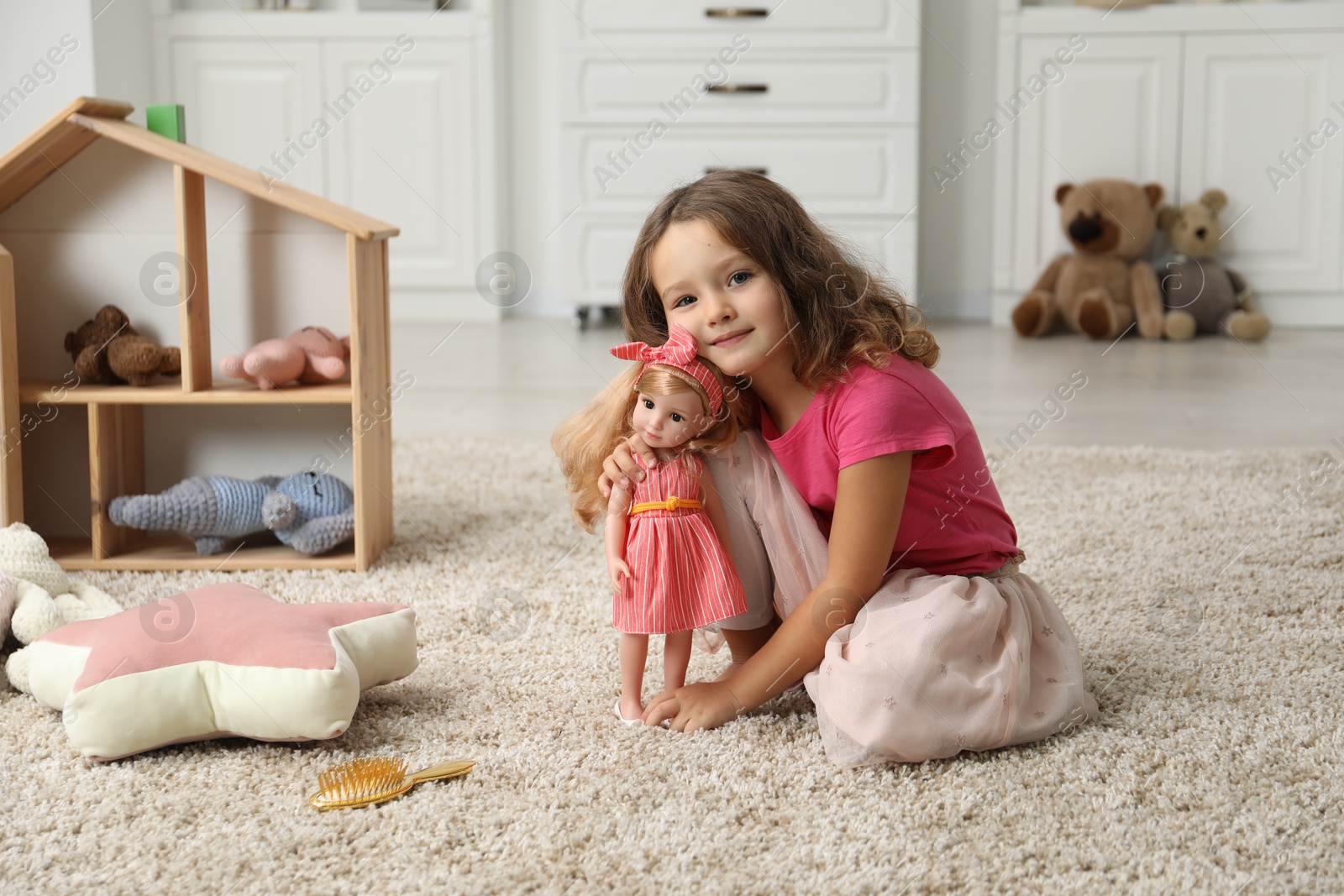 Photo of Cute little girl playing with her doll on floor at home