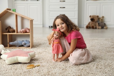 Photo of Cute little girl playing with her doll on floor at home