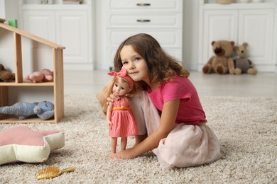 Photo of Cute little girl playing with her doll on floor at home