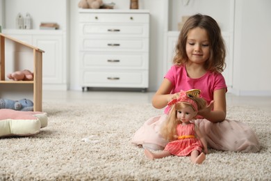 Photo of Cute little girl playing with her doll on floor at home. Space for text