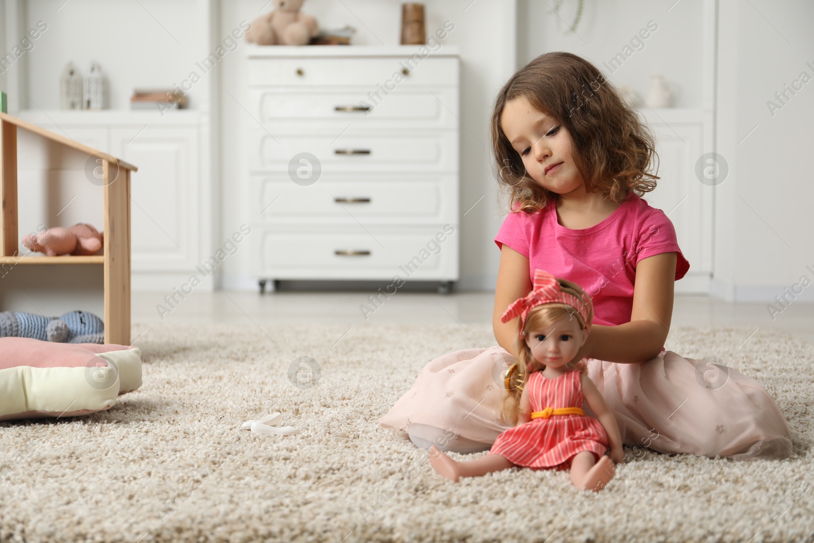 Photo of Cute little girl brushing doll's hair on floor at home. Space for text