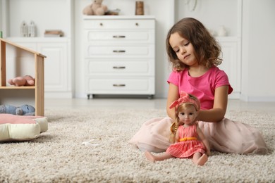 Photo of Cute little girl brushing doll's hair on floor at home. Space for text