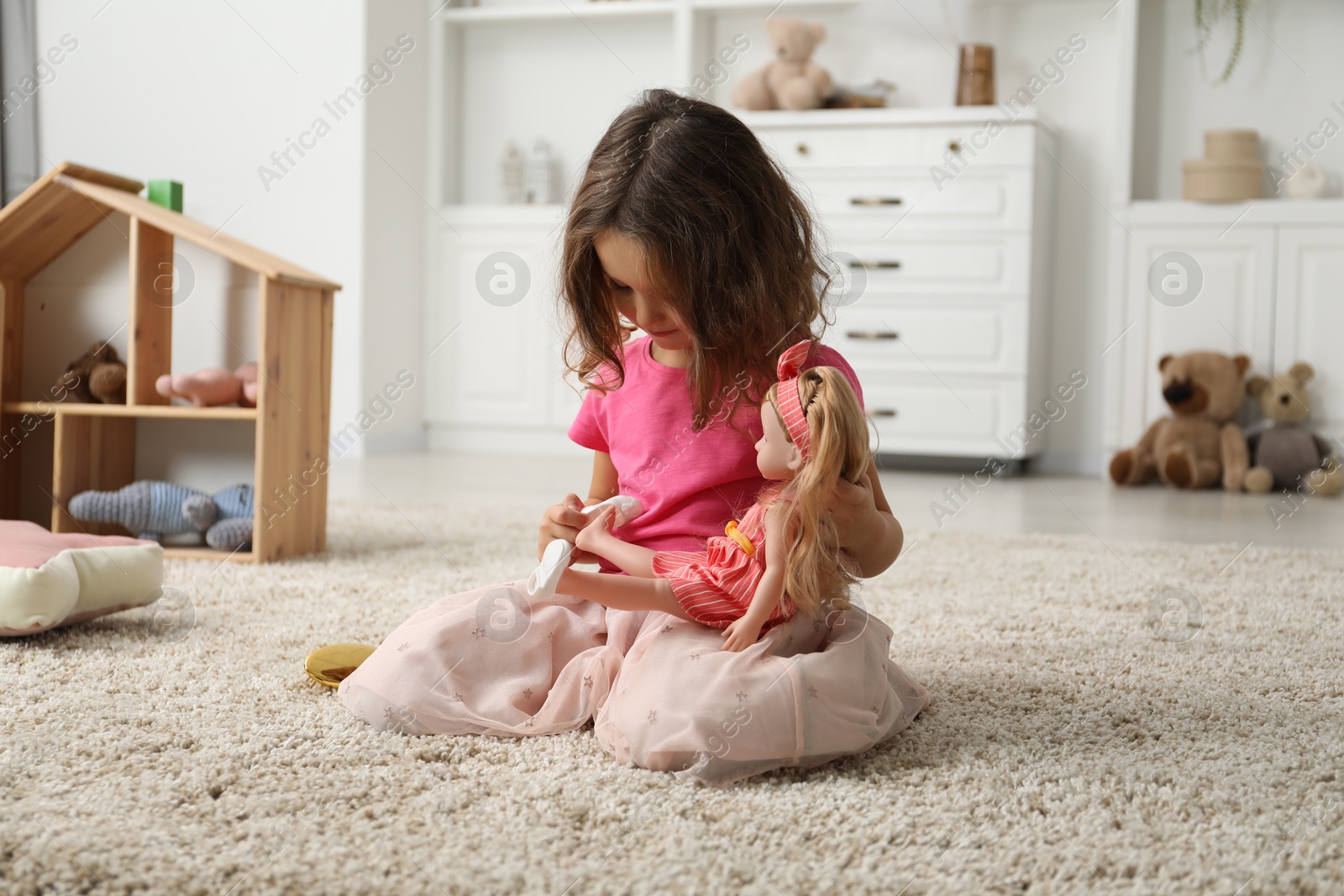 Photo of Little girl playing with her doll on floor at home