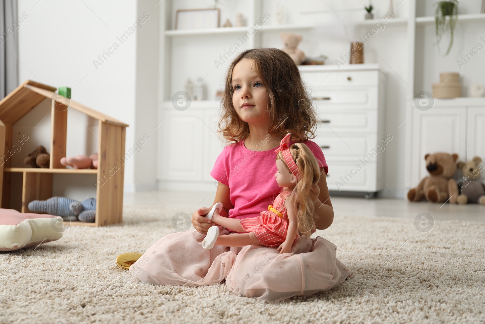 Photo of Cute little girl playing with her doll on floor at home