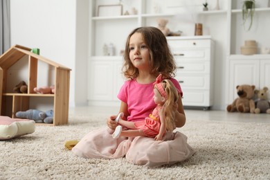 Photo of Cute little girl playing with her doll on floor at home