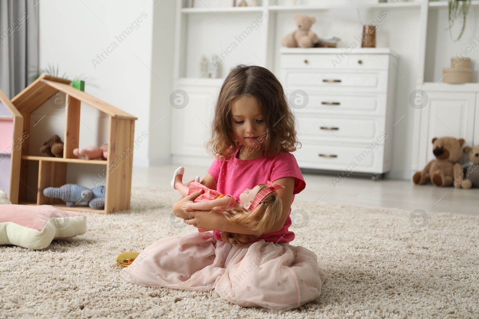 Photo of Cute little girl playing with her doll on floor at home