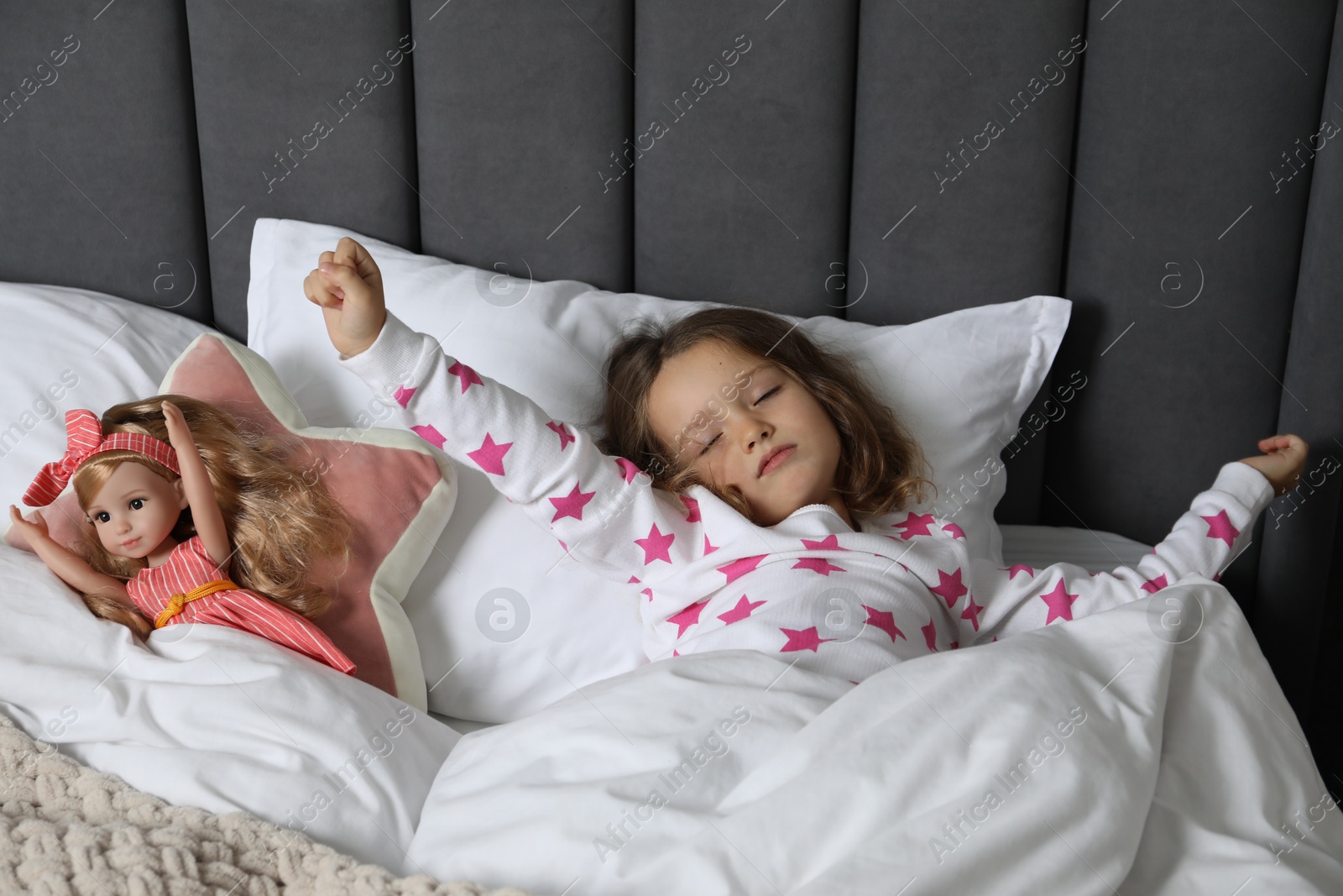 Photo of Cute little girl stretching near her doll in bed