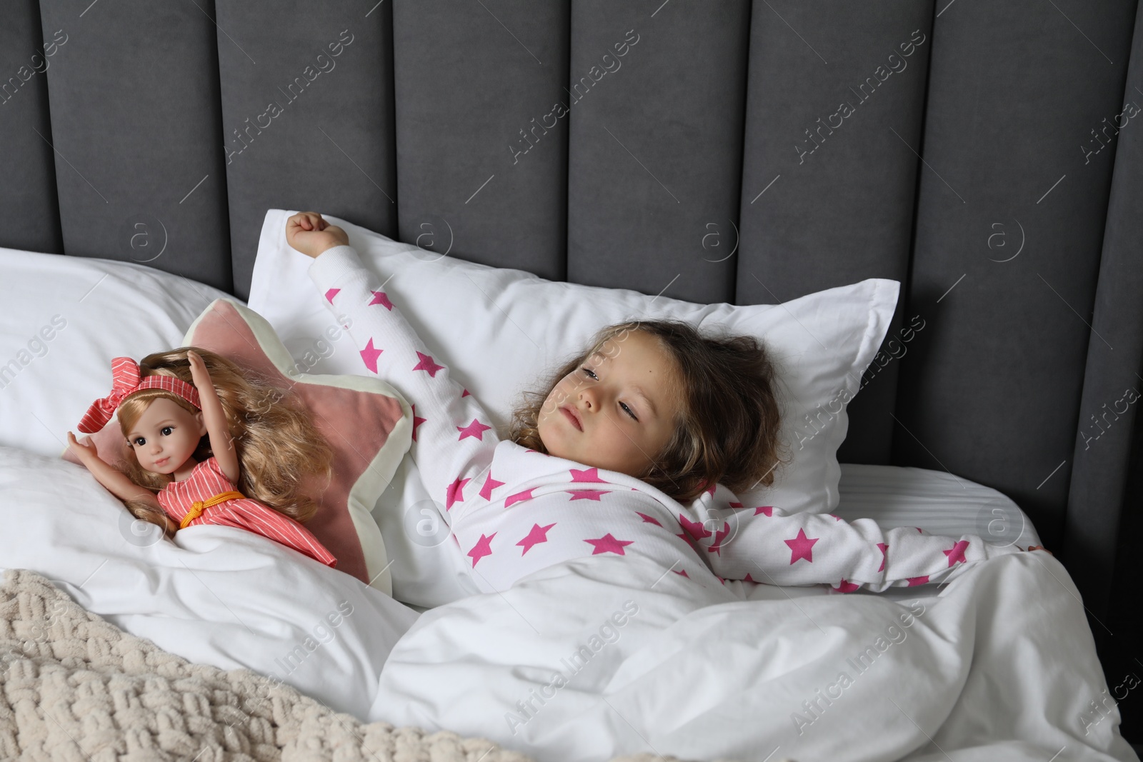 Photo of Cute little girl stretching near her doll in bed