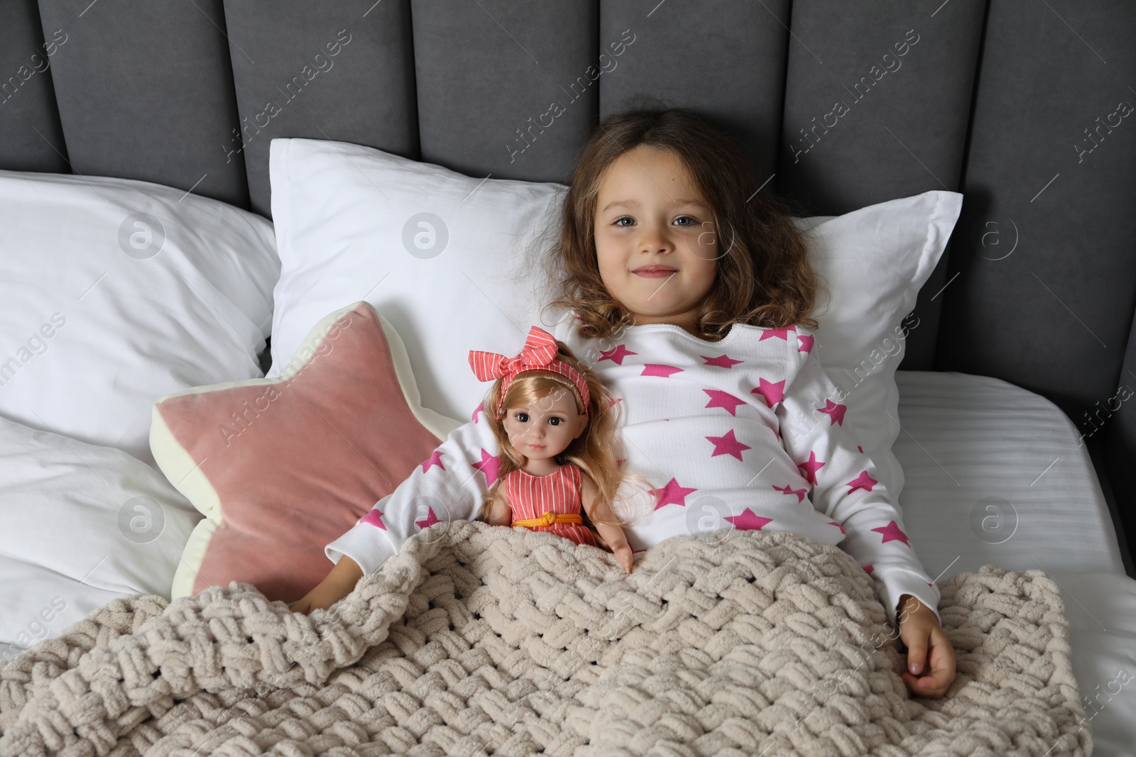 Photo of Cute little girl with doll under blanket in bed