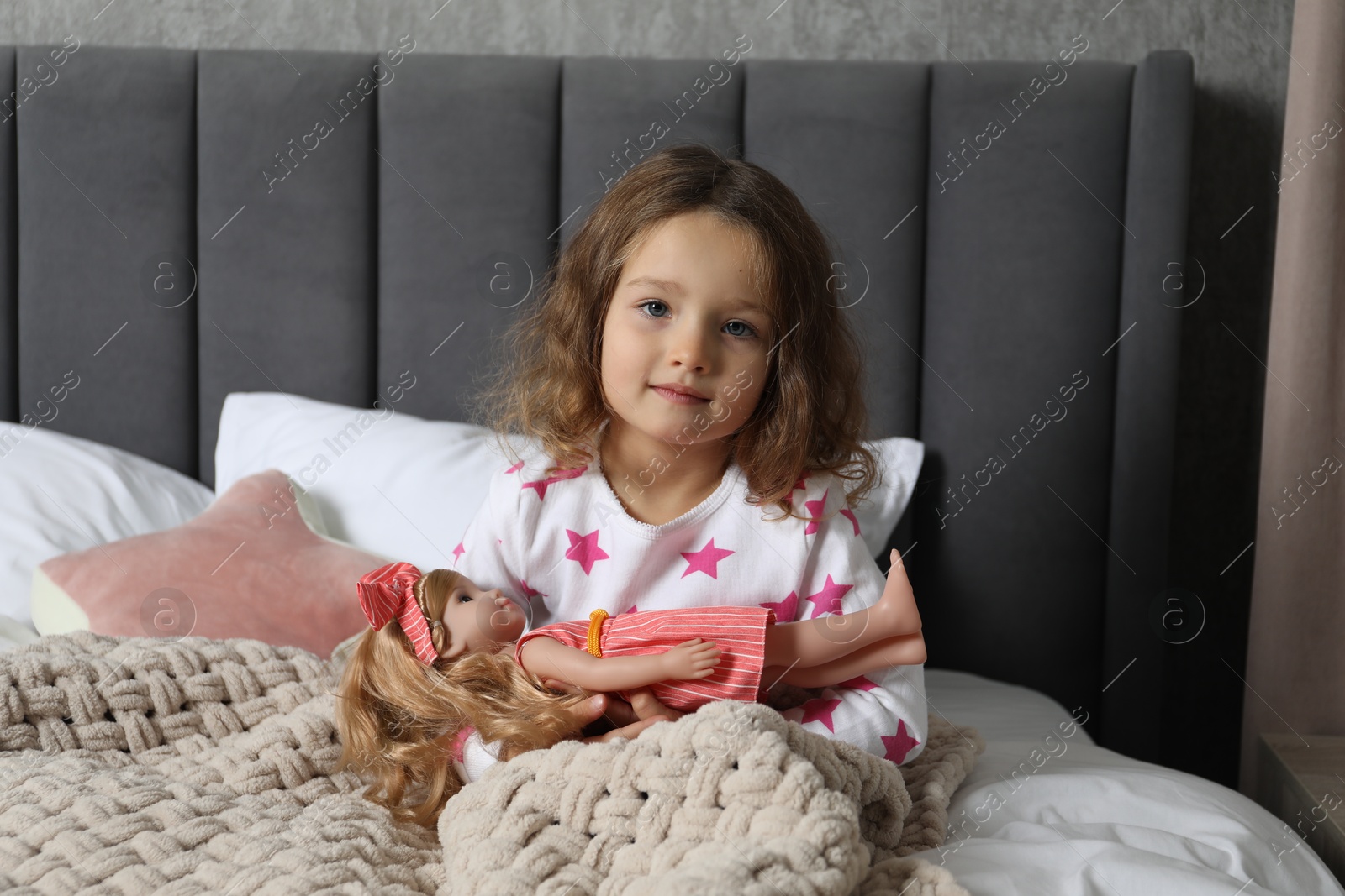 Photo of Cute little girl playing with doll in bed