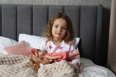 Photo of Cute little girl playing with doll in bed