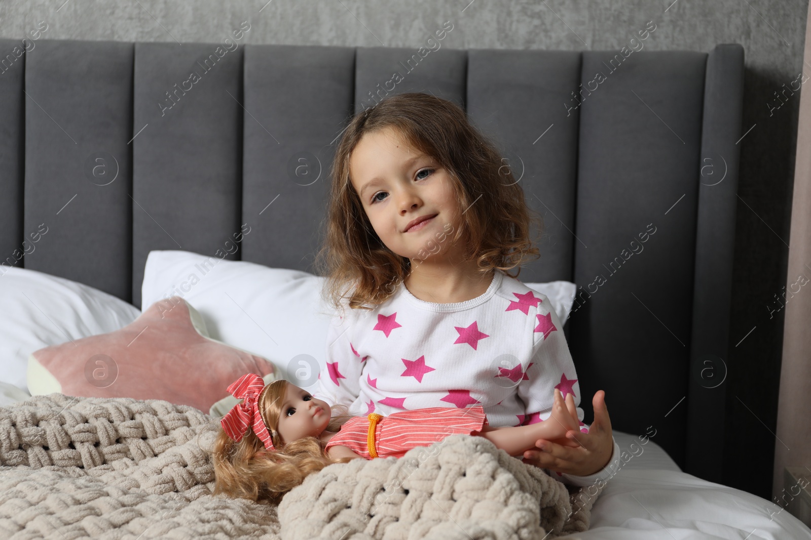 Photo of Cute little girl playing with doll in bed