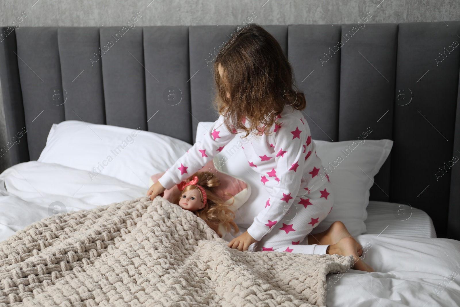 Photo of Little girl playing with doll in bed