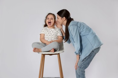 Photo of Teenage girl whispering secret to her cute little sister on white background