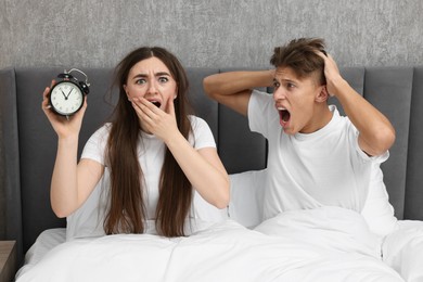 Shocked overslept couple with alarm clock in bed at home