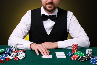 Professional croupier at gambling table with playing cards, casino chips and dice, closeup