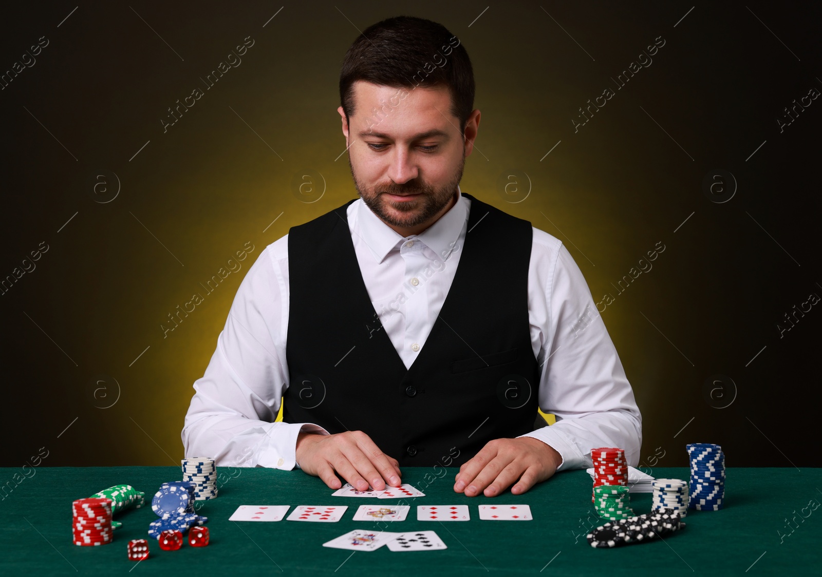 Photo of Professional croupier with playing cards at gambling table on dark yellow background