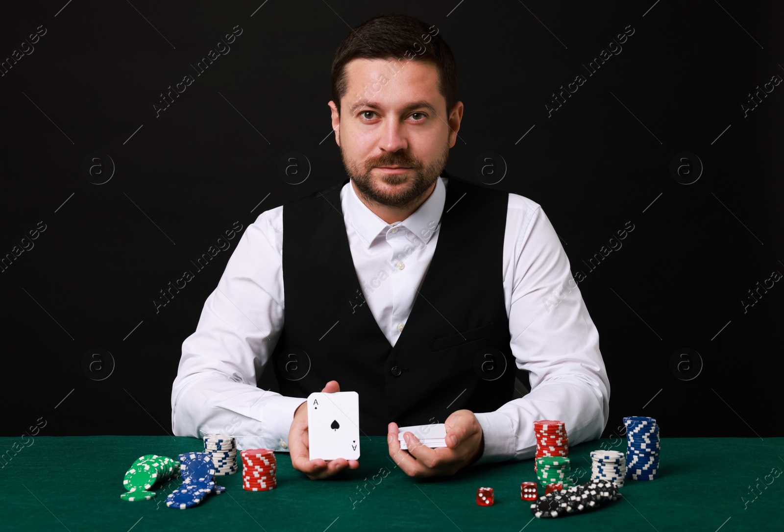 Photo of Professional croupier with playing cards at gambling table against black background