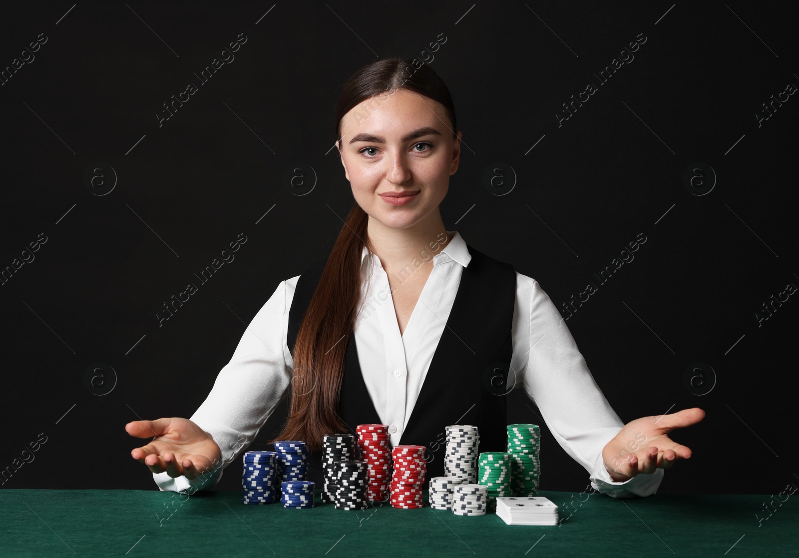 Photo of Professional croupier with casino chips and playing cards at gambling table on black background