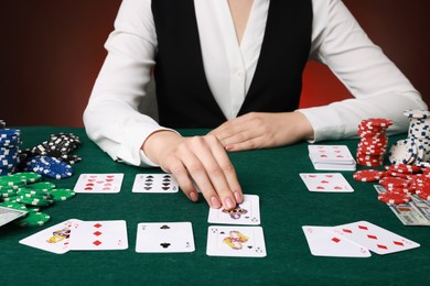 Photo of Professional croupier with casino chips and playing cards at gambling table on color background, closeup