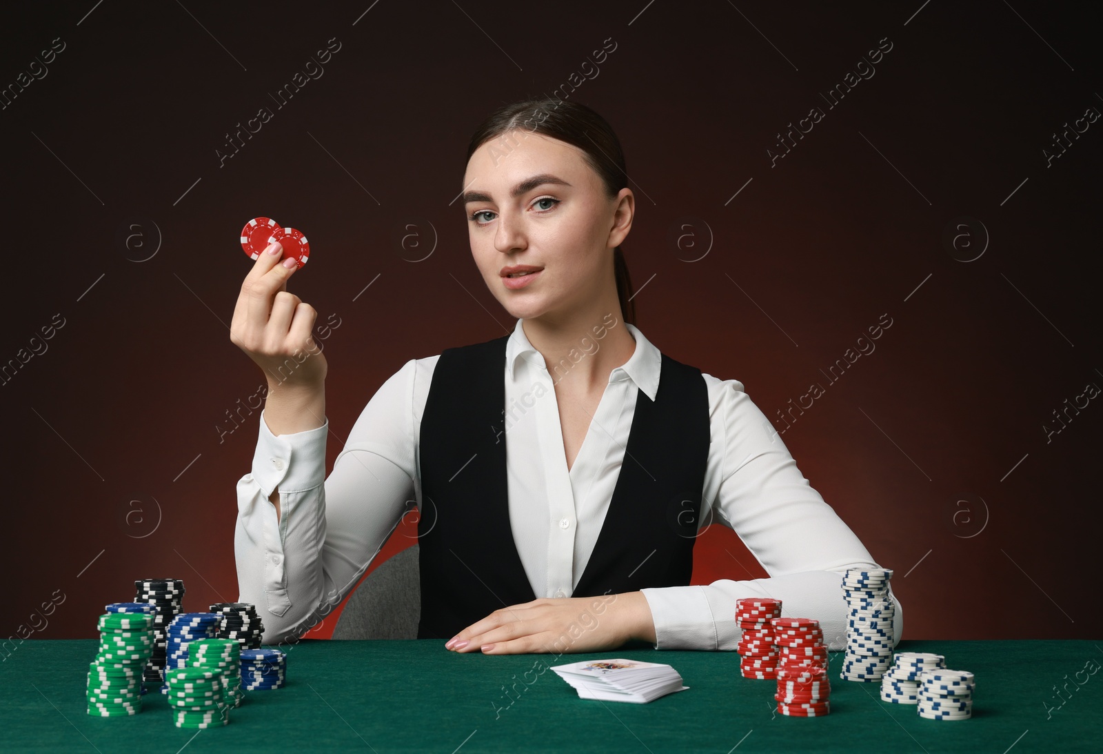 Photo of Professional croupier with casino chips and playing cards at gambling table on color background