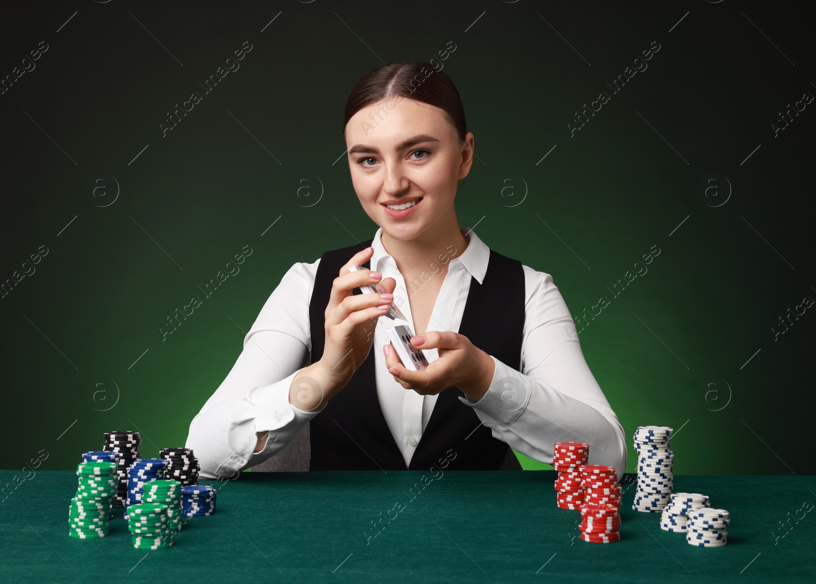 Photo of Professional croupier with chips shuffling playing cards at gambling table on color background