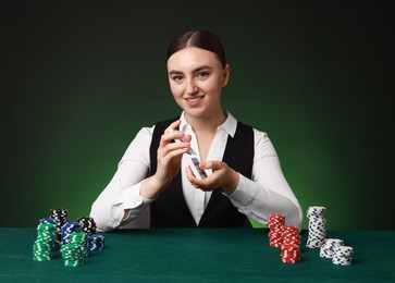 Photo of Professional croupier with chips shuffling playing cards at gambling table on color background