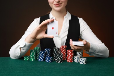 Photo of Professional croupier with casino chips and playing cards at gambling table on color background, closeup