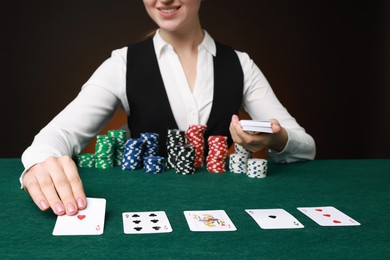 Photo of Professional croupier with casino chips and playing cards at gambling table on color background, closeup