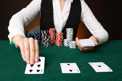 Photo of Professional croupier with casino chips and playing cards at gambling table on color background, closeup