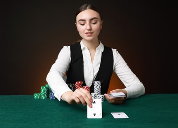 Professional croupier with casino chips and playing cards at gambling table on color background