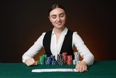 Photo of Professional croupier with casino chips and playing cards at gambling table on color background