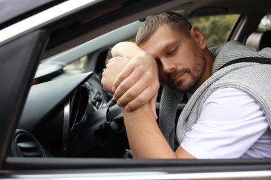 Photo of Tired man sleeping on steering wheel in car