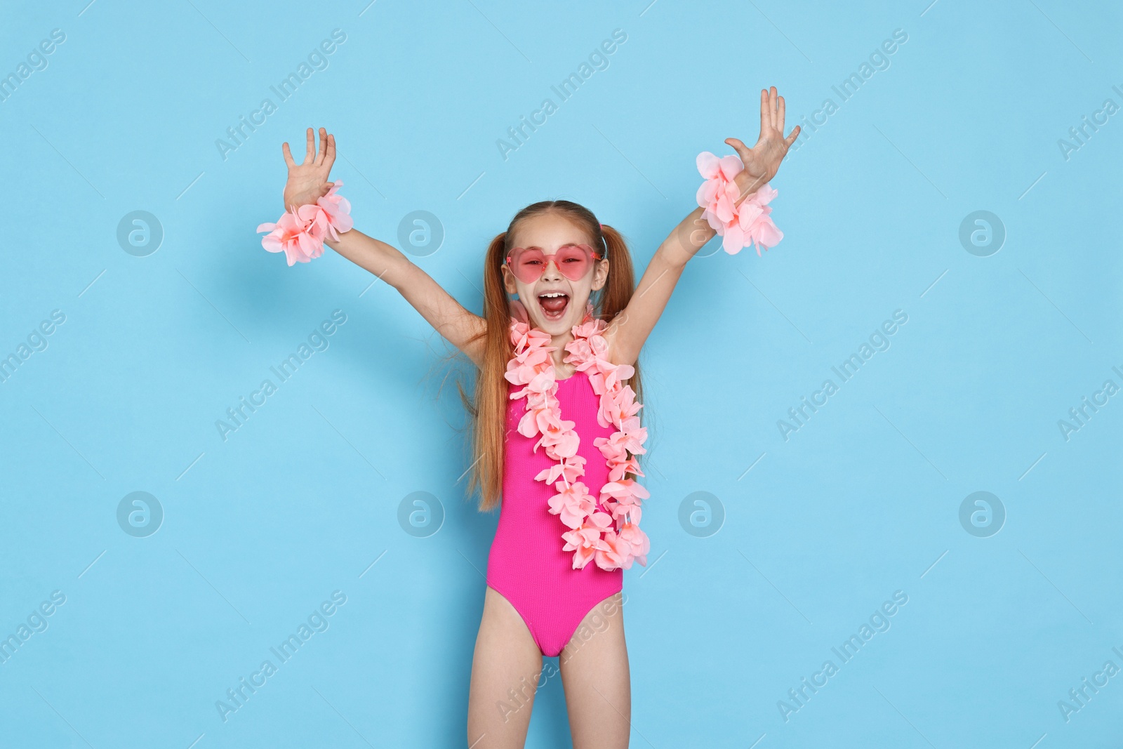 Photo of Happy little girl in beachwear and wreaths of flowers on light blue background